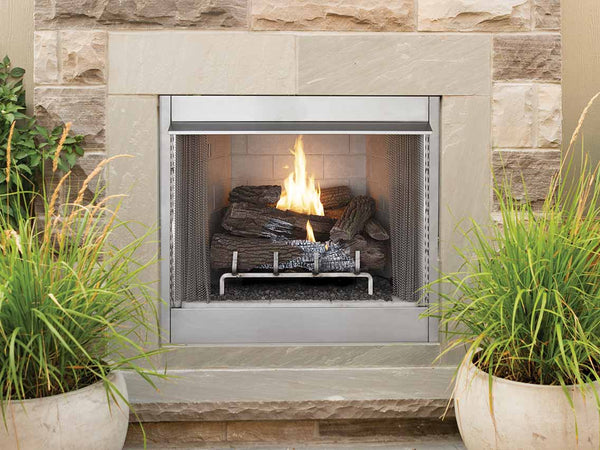 Modern outdoor fireplace with a stainless steel frame, warm fire, and decorative stone surround, accented by lush green potted plants.