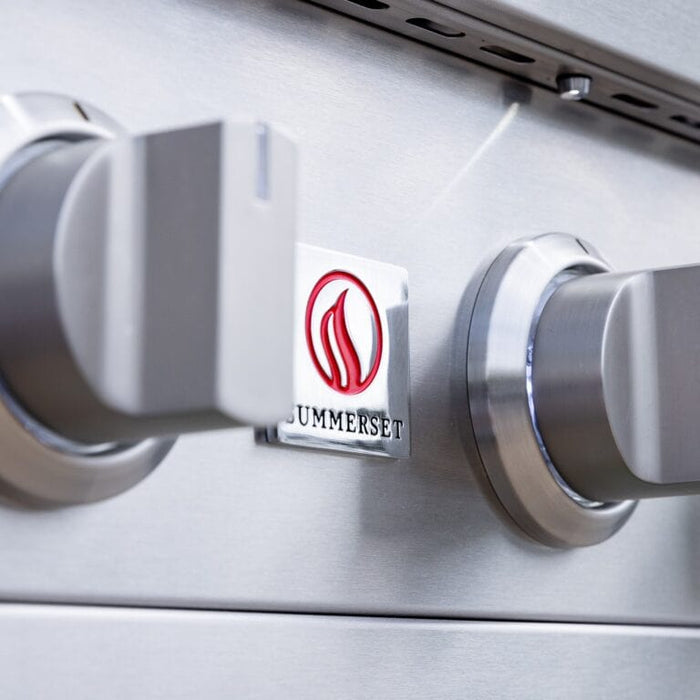 Close-up of stainless steel grill control knobs and brand logo on front panel.