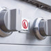 Close-up of stainless steel grill control knobs and brand logo on front panel.