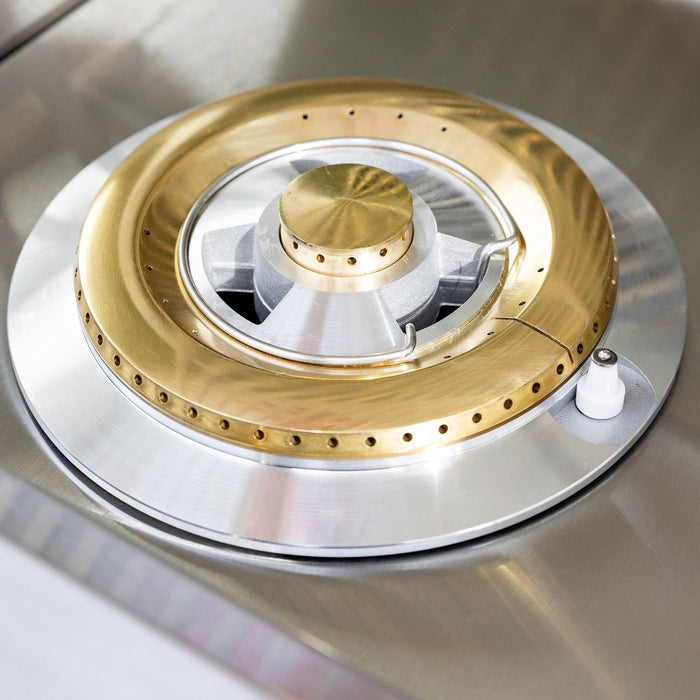Close-up of brass and stainless steel gas burner showing precision flame ports and ignition system for outdoor cooking.