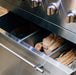 Close-up of a stainless steel grill drawer containing wood logs and charcoal, designed for versatile outdoor cooking options.