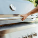 Close-up of a person opening a stainless steel grill lid with a built-in thermometer and sleek handle, showcasing modern design.