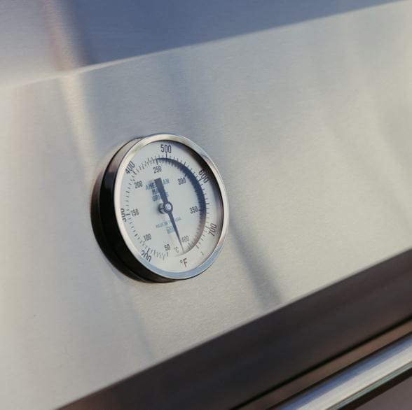 Close-up of a built-in thermometer on a stainless steel grill lid, displaying precise temperature measurements for outdoor cooking.