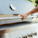 Person gripping the handle of a stainless steel grill with a built-in thermometer, preparing to open the lid in an outdoor setting.
