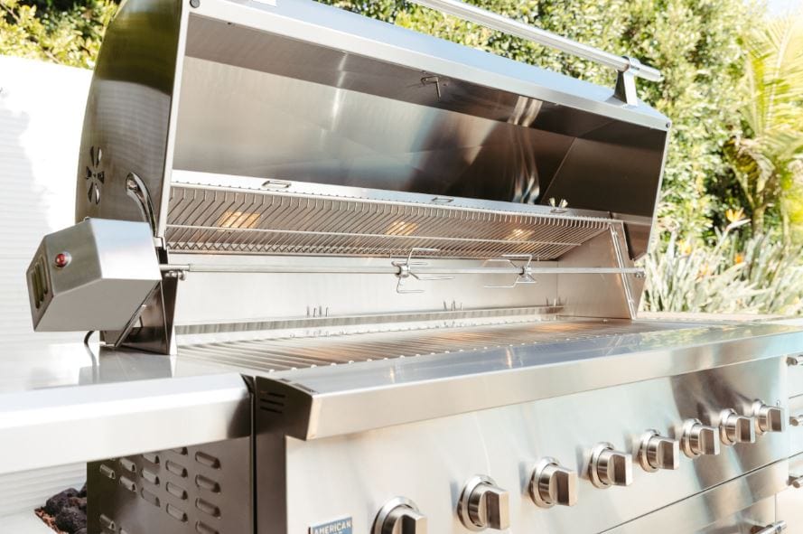 Open stainless steel grill with multiple control knobs, spacious cooking grates, warming rack, and side burner in an outdoor setting.
