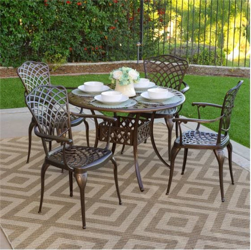 Elegant outdoor dining set with a round table and four lattice-back chairs placed on a patterned rug in a lush garden patio setting.