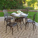 Elegant outdoor dining set with a round table and four lattice-back chairs placed on a patterned rug in a lush garden patio setting.