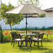 Outdoor patio dining set with a round metal table, four cushioned chairs, and a beige umbrella, set in a backyard with flowers and greenery.