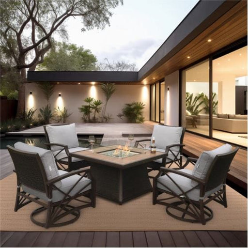 A square fire pit table with a glass enclosure, surrounded by cushioned chairs on a patio with a pool in the background.