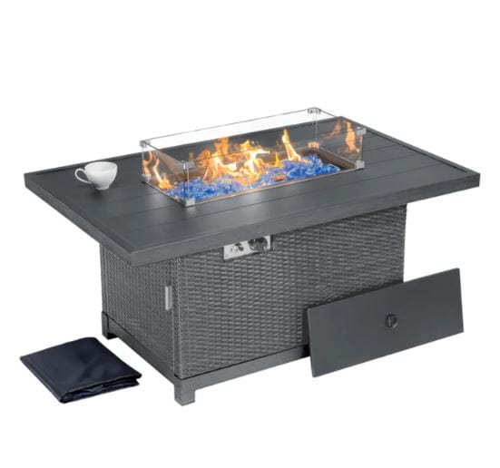 Rectangular outdoor fire pit table with a glass wind guard, blue fire glass, a wicker base, side access panel, and included cover.