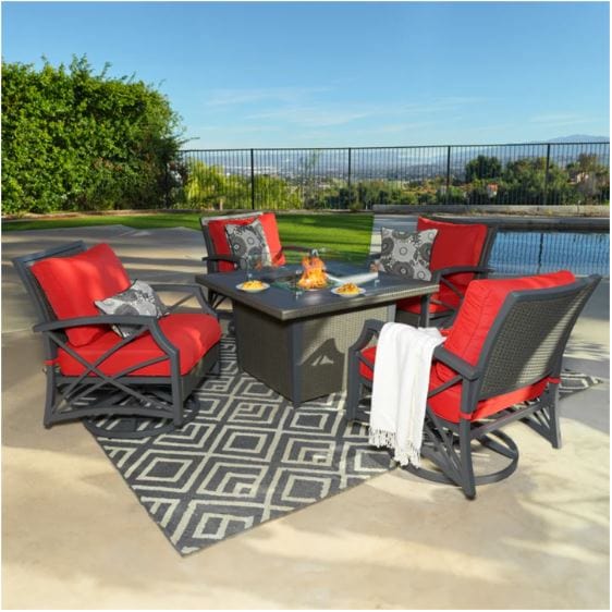 Outdoor fire pit table set with a square fire pit, red cushioned swivel chairs, patterned throw pillows, and a geometric outdoor rug by a pool.