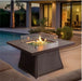 Modern outdoor fire pit table with wicker base and tempered glass wind guard, set on a patio near a pool, creating a cozy ambiance.