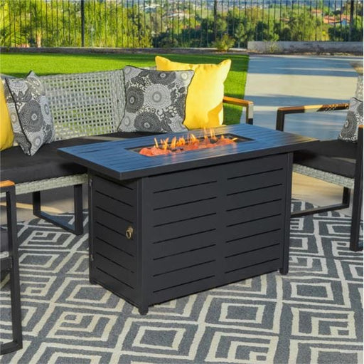 Modern black fire pit table on a patterned outdoor rug, surrounded by stylish patio furniture with decorative pillows, set in a backyard.