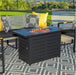 Modern black fire pit table on a patterned outdoor rug, surrounded by stylish patio furniture with decorative pillows, set in a backyard.