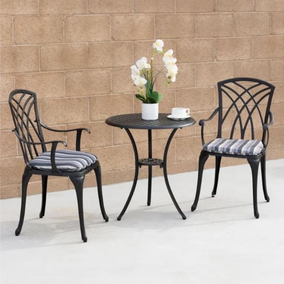 Elegant 3-piece outdoor patio set featuring a round black table with a floral centerpiece and two cushioned chairs against a brick wall.