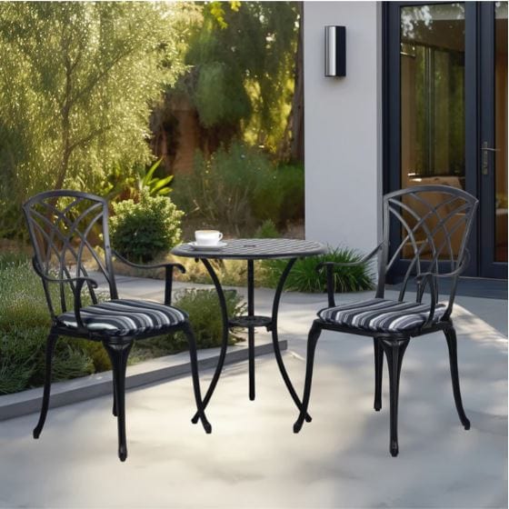 Elegant outdoor patio set with a round table and two cushioned chairs placed on a modern patio surrounded by greenery and glass doors.