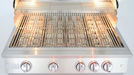 Stainless steel gas grill with wide cooking grates, upper warming rack, bright interior lights, and five illuminated control knobs.
