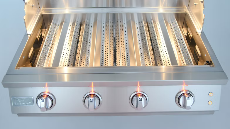 Stainless steel gas grill interior featuring perforated flame tamers, bright lighting, and four illuminated control knobs for precise heat control.