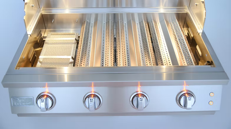 Stainless steel gas grill interior with perforated flame tamers, a built-in smoker box, and four illuminated control knobs for precision grilling.