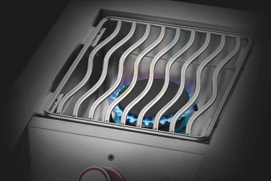 Close-up of a stainless steel outdoor burner with wavy grill grates, blue flame visible beneath for precise and efficient cooking.