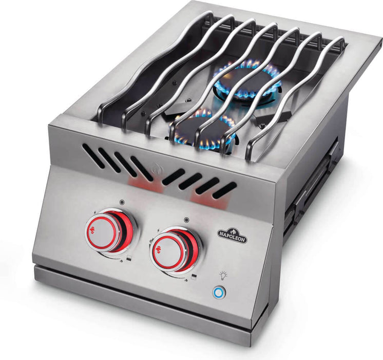 Stainless steel double burner with wavy grill grates, visible blue flame, red-lit control knobs, and push-button ignition for cooking.