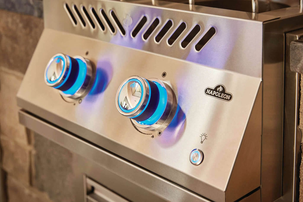 Close-up of a stainless steel outdoor burner with blue-lit control knobs, side vents, and a sleek design, integrated into a kitchen setup.