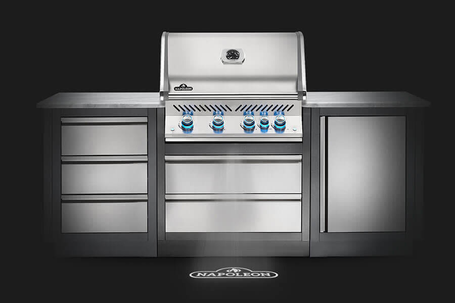 Stainless steel built-in gas grill with a closed lid, blue-lit knobs, flanked by matching storage drawers and cabinets in a sleek design.