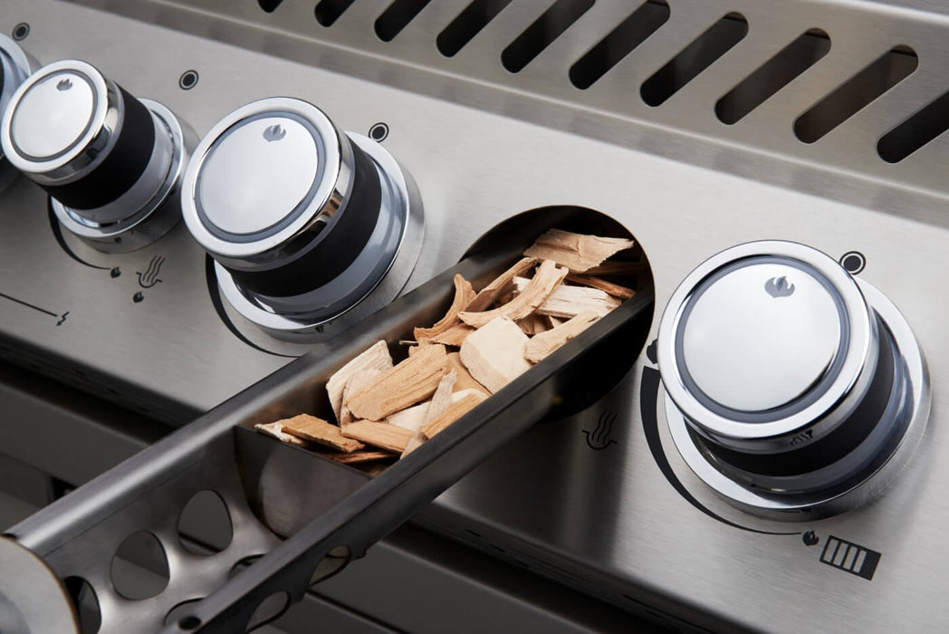 Close-up of a gas grill's stainless steel control panel with a smoker tube filled with wood chips inserted beside control knobs.