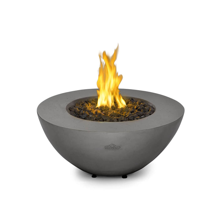 Modern round fire bowl with flames rising from a bed of black lava rocks, featuring a minimalist gray design on a white background.