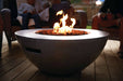 Contemporary round fire bowl with flames glowing over lava rocks, surrounded by people seated on a wooden deck in a cozy evening setting.