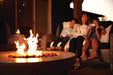 Family sitting on an outdoor wicker couch, enjoying a cozy fire pit in the foreground, with warm ambient lighting on a patio.