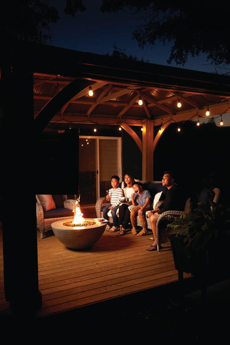 Family sitting together on a cozy deck at night under string lights, enjoying the warmth of a fire pit in a modern outdoor setting.