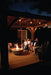 Family sitting together on a cozy deck at night under string lights, enjoying the warmth of a fire pit in a modern outdoor setting.