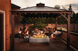 Group of people enjoying an evening around a modern fire table under a gazebo with string lights, seated on cushioned outdoor chairs.