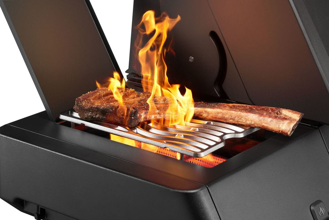 A sizzling tomahawk steak being seared on a high-heat infrared side burner with flames rising, surrounded by a black grill housing.