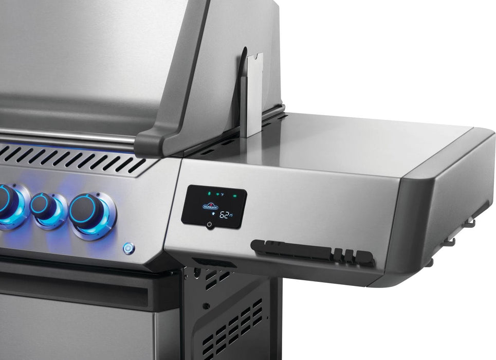 Side view of a grill showing control knobs with blue lighting, a digital display panel, utensil hooks, and a sleek stainless steel finish.