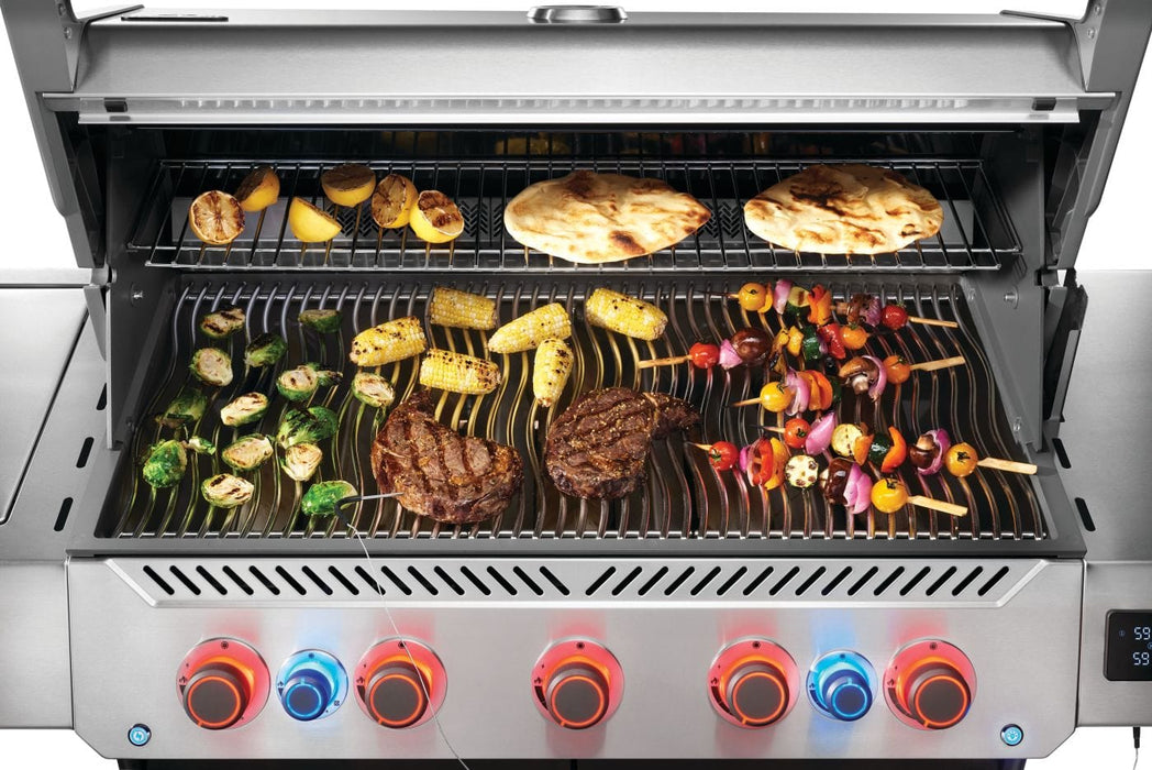 Grill with red and blue illuminated knobs, cooking kebabs, corn, vegetables, and flatbreads on open grates under a stainless steel lid.