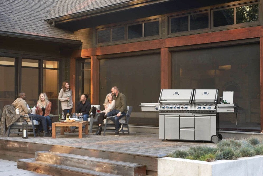 Outdoor patio scene with a group of people enjoying drinks and conversation, featuring a large stainless steel grill on the deck