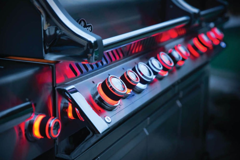 Close-up of illuminated red control knobs on a stainless steel outdoor grill, highlighting precision controls and sleek design features