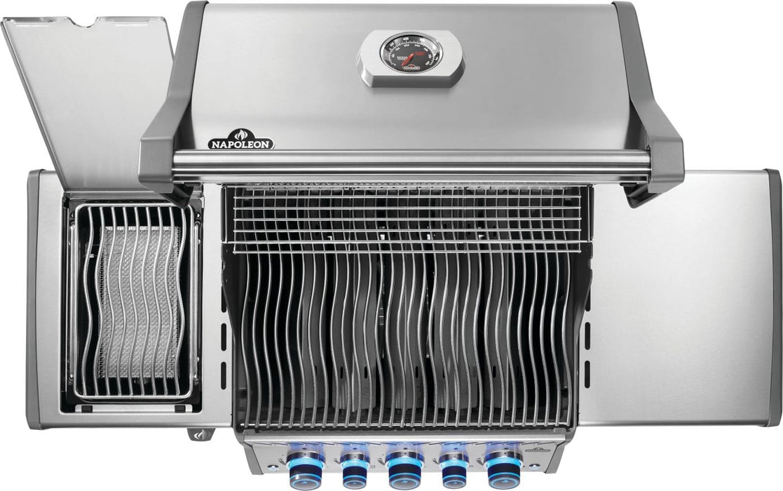 Top view of a stainless steel grill with open side burner, wavy cooking grates, warming rack, and illuminated control knobs.