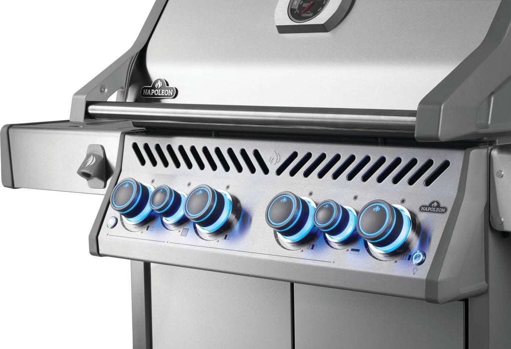 Close-up of a stainless steel grill control panel with illuminated blue knobs, sleek handle, and side burner ignition button.