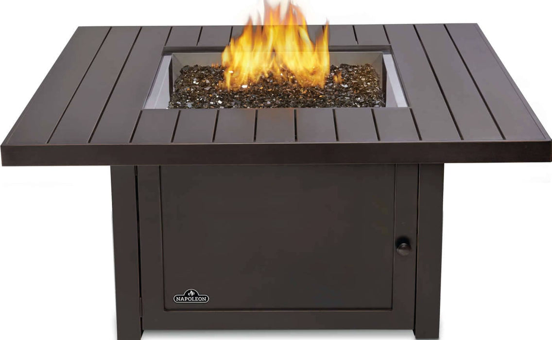 Square fire pit with a sleek metal finish, featuring a centered flame surrounded by decorative black glass stones.