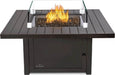 Square fire pit with black metal frame, central flame surrounded by glass panels, and decorative black stones, designed for outdoors.