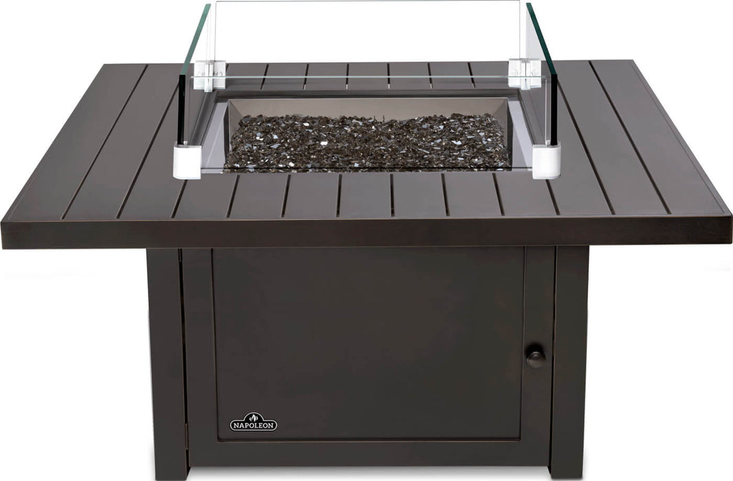 Square fire pit with a black metal frame, central section filled with black stones, and protective glass panels on each corner.