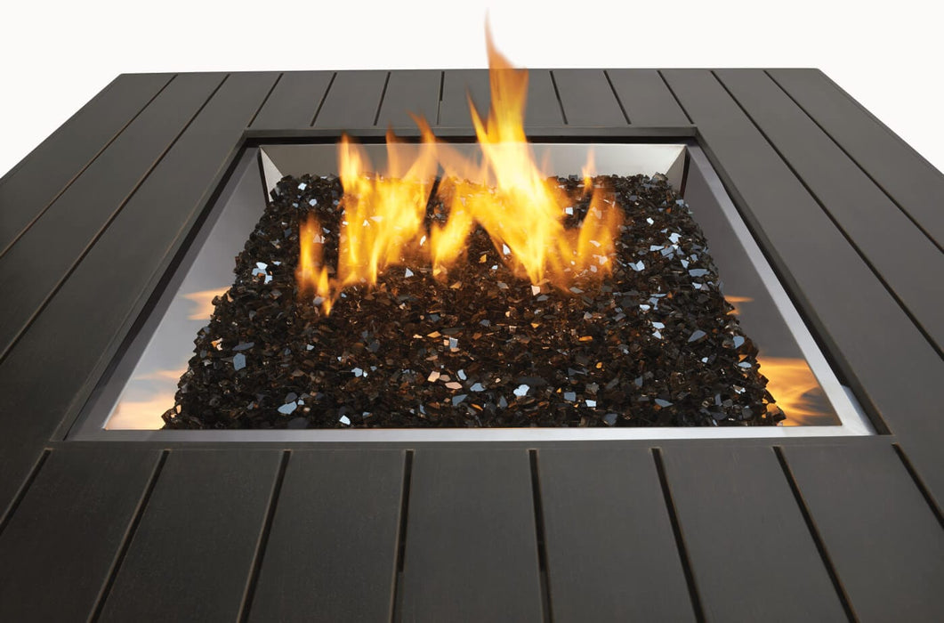 Close-up of a square fire pit featuring a black stone bed with vibrant flames, surrounded by a sleek black slatted metal frame.