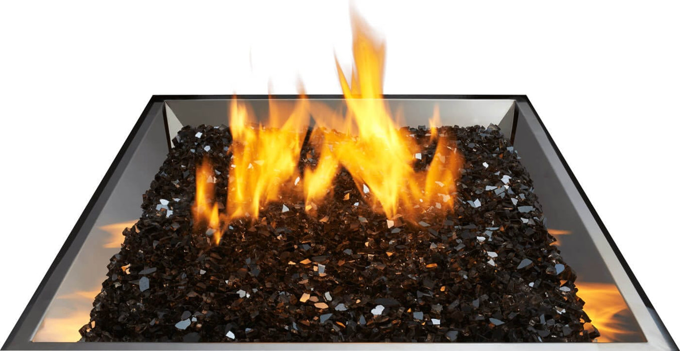 Close-up view of a square fire pit with glowing flames emerging from a bed of reflective black stones, surrounded by metal edges.