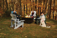 Outdoor autumn scene with people seated in Adirondack chairs around a fire table, surrounded by vibrant fall foliage and trees.