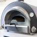 Stainless steel outdoor pizza oven with built-in thermometer, control knobs, and partially open door handle.
