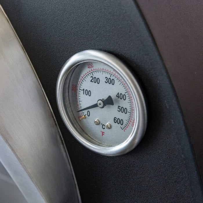 Close-up of built-in stainless steel temperature gauge on an outdoor pizza oven showing Fahrenheit and Celsius readings.