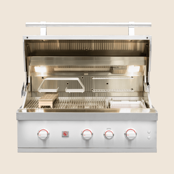 Open stainless steel gas grill showing cooking grates, warming rack, interior lights, and control knobs on the front panel.
